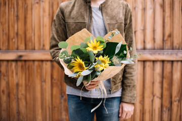 Very nice young man holding big and beautiful mono bouquet of fresh yellow sunflowers, cropped...