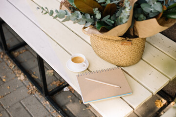 Delicious fresh morning espresso coffee cup standing on the wooden bench with a basket of eucalyptus and a paper notepad