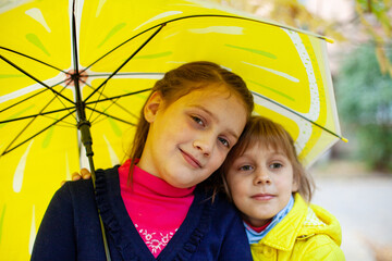 Two children with   yellow umbrella stand side by side on   street on   autumn day.