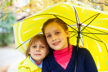  Two girls of 7 and 10 years old   hugging under   yellow umbrella in autumn.
