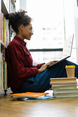Side view of the focused multiracial school girl studying with laptop while preparing for test exam or doing homework. Teenage student learning assignment making notes. Teen education concept