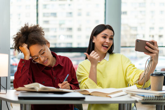 Waist up portrait view of the caucasian overjoyed woman gesturing while making selfie with her multiracial classmate. Studying concept