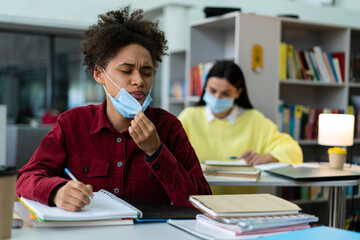 Portrait view of the multiracial woman lowers the mask while studying with her classmates at the library during the pandemic