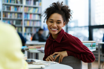 Waist up portrait view of the multiracial woman looking at the camera with toothy smile while spending time at the school library