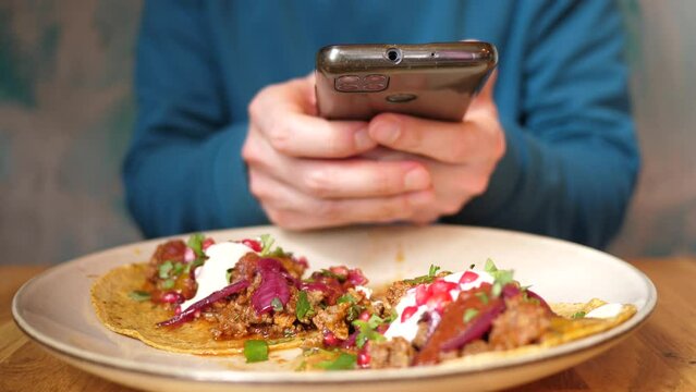 Man taking smartphone picture of tacos dish in restaurant for social media food photo