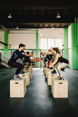 Group of sportive people training on wooden cubes together in modern gym equipped for crossfit. Sportspeople doing squats on wooden cubes during training session.