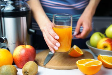 Woman's hands holds glass with freshly squeezed multivitamin juice. Natural and healthy juices at home. Close-up. Selective focus.