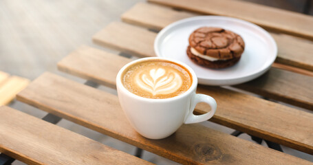A cup of aromatic cappuccino and delicious chocolate cookies on a table in a street cafe. Coffee break on a summer sunny day. Close-up. Copy space.