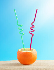 Summer concept. Cocktail in an orange with two straws on the sand.