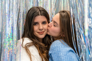 Couple of friends looking at the camera between a curtain of glitter and silver and colored reflections and smiling happily