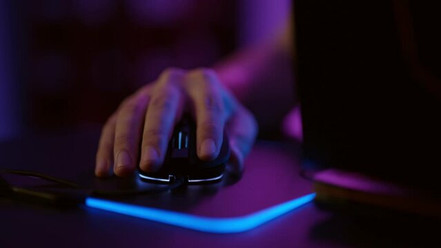 Close-up hands of gamer playing video game using illuminated mouse.Male hand using mouse. Background with neon lights.