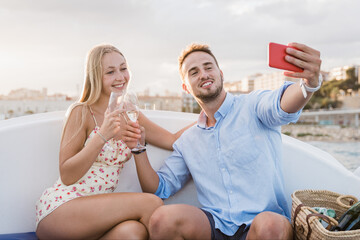 Happy couple having fun doing selfie inside luxury sail boat during summer vacations - Focus on...