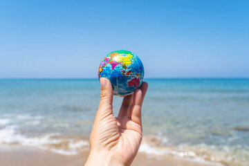 Toy globe in female hand on the sand of beach with sea wave background. World travel concept.