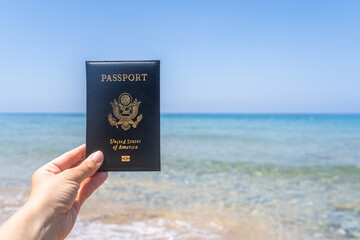 Woman holding american passport in a cover opposite sea wave beach. Concept of summer travel, tourism, holiday.