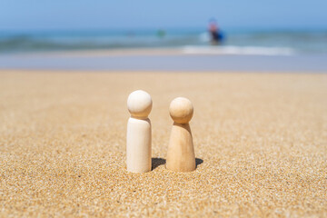 Fototapeta na wymiar Wooden two figures of people on the sand of beach with sea view. Concept of happy couple on holiday.