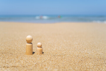 Wooden two figures of people on the sand of beach with sea view. Concept of happy children on holiday.