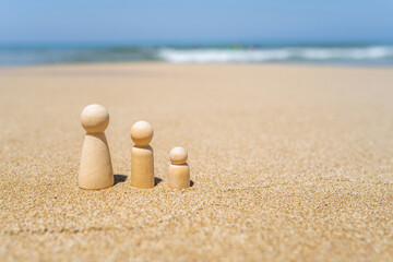 Wooden three figures of people on the sand of beach with sea view. Concept of happy family with two kids on holiday.
