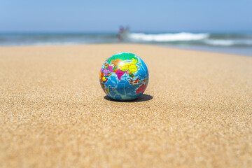 Fototapeta na wymiar Toy globe on the sand of beach with sea wave background. World travel concept.