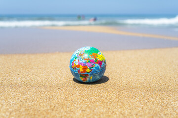 Fototapeta na wymiar Toy globe on the sand of beach with sea wave background. World travel concept.