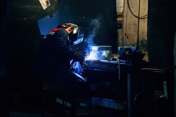 Factory worker in protective mask welding iron parts, close up