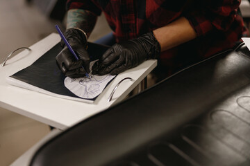 Close up of female hands of tattoo artist drawing sketch for tattoo on paper