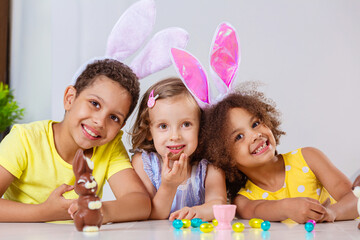 three children in bright clothes eating Easter eggs