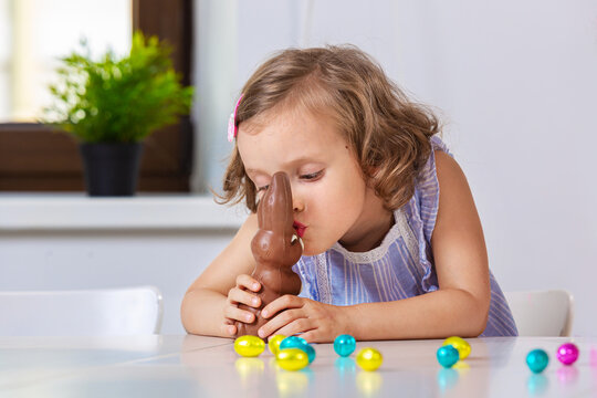 Girl kissing Easter chocolate bunny sitting at home