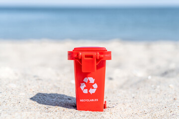 Red colored trash can recyclables with paper, plastic, glass and organic waste suitable for recycling on sandy beach. Segregate waste, sorting garbage