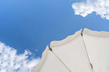 Bottom view on white beach or pool umbrella and blue sky with small cloudy. Copy space. Holiday,...