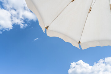 Bottom view on white beach or pool umbrella and blue sky with small cloudy. Copy space. Holiday, vacation, travel concept - 486338728