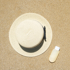 Fototapeta na wymiar Summer straw hat and sunscreen lying on sand of beach. Travel, holiday, summertime concept. Copy space. Top view. Flat lay