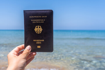 Woman holding Deutsch passport in a cover opposite sea wave beach. Concept of summer travel, tourism, holiday.