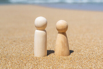Wooden two figures of people on the sand of beach with sea view. Concept of happy couple on holiday.
