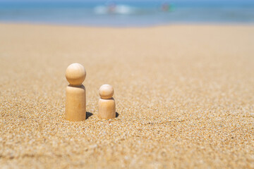 Wooden two figures of people on the sand of beach with sea view. Concept of happy children on holiday.