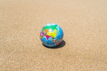 Toy globe on the sand of beach. World travel concept.