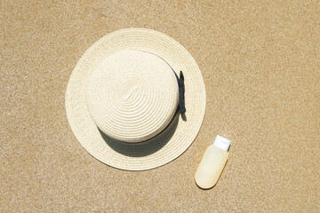 Fototapeta na wymiar Summer straw hat and sunscreen lying on sand of beach. Travel, holiday, summertime concept. Copy space. Top view. Flat lay
