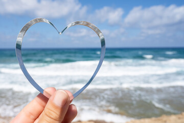 Sea view through shape of heart in the female hand of tropical beach. Valentines day. Holiday, vacation concept. Creative, background, copy space, travel, summer.