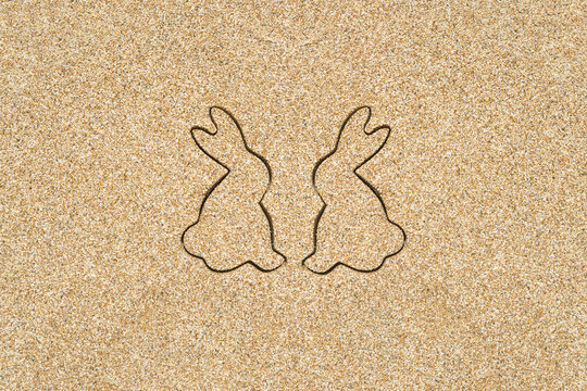 Drawing creative two easter bunny on the sand on the beach.