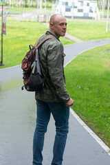 A sporty man in a military jacket and with a backpack in the park. Vertical photo.