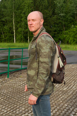 A sporty man in a military jacket and with a backpack. Vertical photo.