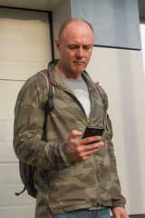 A sporty man in a military jacket with a mobile phone in his hands sends a message on the street