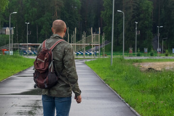A sporty man in a military jacket and with a backpack. View from the back. Empty space for the text.
