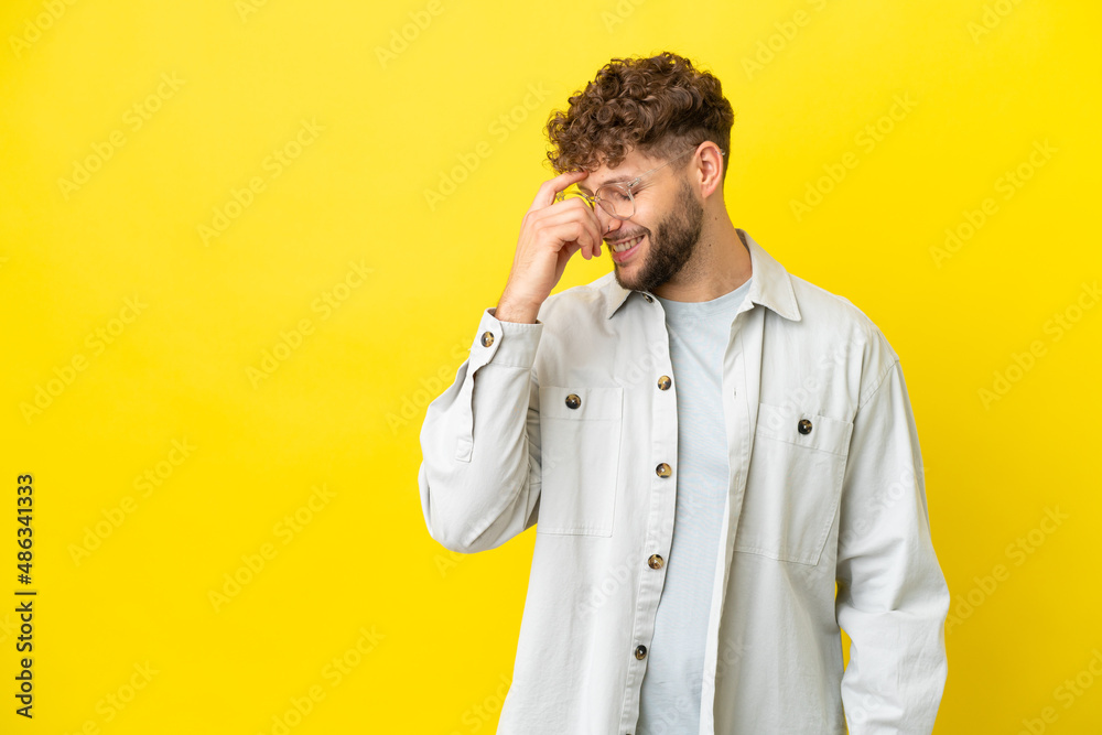 Wall mural Young handsome caucasian man isolated on yellow background laughing