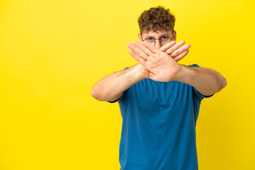Young handsome caucasian man isolated on yellow background making stop gesture with her hand to stop an act