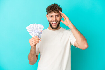 Young caucasian man taking a lot of money isolated on blue background with surprise expression