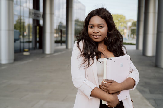 Outside office, corporation company businesswoman dressed in jacket stands in front of business center, glass building, holding folder with documents goes to take them to boss