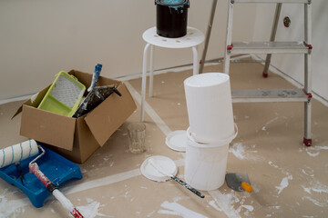 The mess after a renovation. A set of rollers and brushes for painting walls on a cardboard protected floor together with a paint tray, buckets, ladder