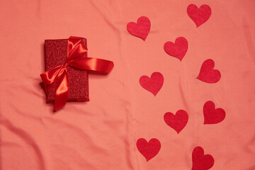 Red gift box with red bow and hearts around on pink silk background. Valentine day concept