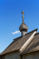The wooden roof of the Orthodox chapel with a small wooden dome and a cross on it. Carved. Gray tree. Folk architecture. Clear blue sky. Daylight.