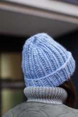 
A handmade hat of very berry color on a girl's head. The girl straightens a fashionable woolen hat with her hands on her head